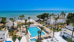 A resort with a central swimming pool, palm trees, and a view of the sea. - Hari Club Beach Resort (Aghir)