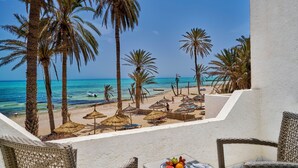 A beach view with palm trees, a table with fruit, and a chair. - Hari Club Beach Resort (Aghir)