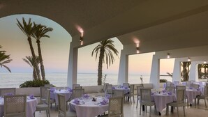 A restaurant with round tables and wicker chairs, overlooking the sea. - Hari Club Beach Resort (Aghir)