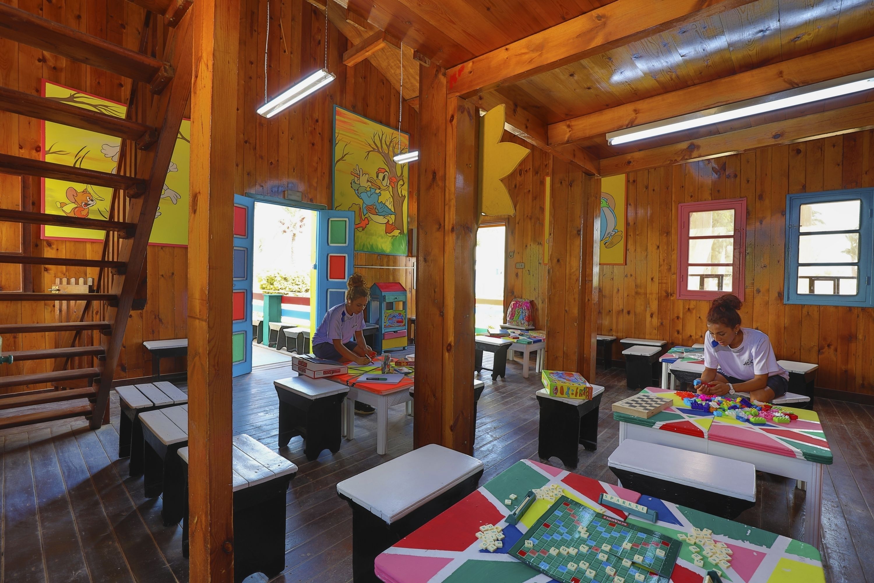 A wooden interior with tables and benches, artwork on the walls, and a ladder.