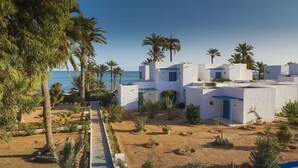 A coastal resort with white buildings, palm trees, and a sandy beach. - Hari Club Beach Resort (Aghir)