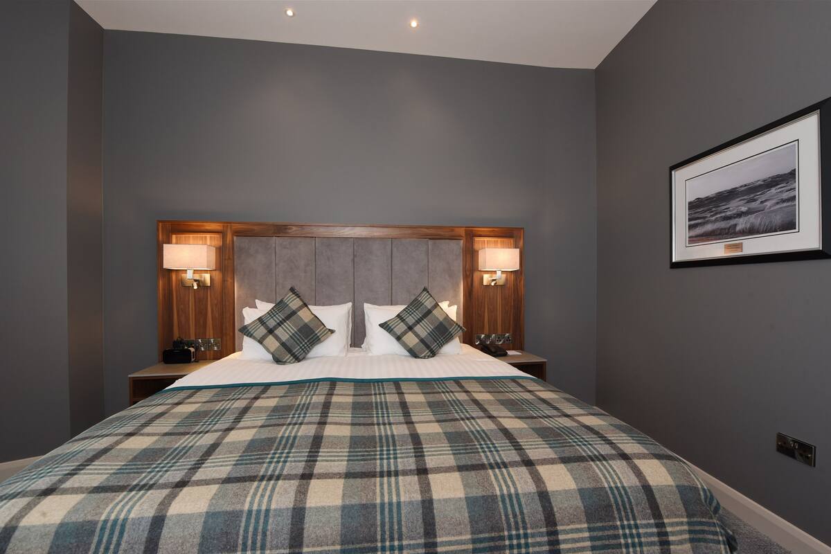 Quarto de hotel com uma cama grande, duas mesas de cabeceira, uma cabeceira e um quadro na parede.
