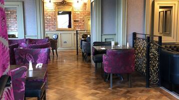 A restaurant with wooden flooring, purple floral chairs, and a brick wall with a mirror.