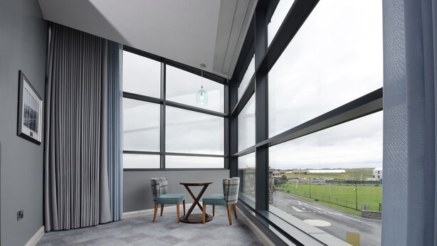 A room with large windows, a view of a road, a table with chairs, and a hanging light fixture. - Golflinks Hotel (Portrush)
