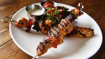 A plate of grilled chicken skewers with a side salad and a small bowl of sauce.