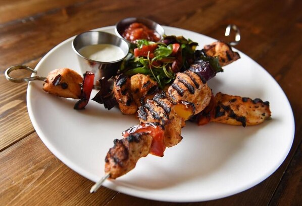 A plate of grilled chicken skewers with a side salad and a small bowl of sauce. - Golflinks Hotel (Portrush)