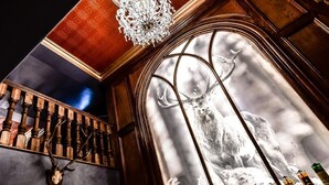 A bar area with a wooden staircase, a mounted deer head, and a wall with a snowy mountain scene and liquor bottles. - Golflinks Hotel (Portrush)
