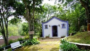 A small white building with a blue roof and a door, surrounded by greenery and trees. - Hospedaria da Villa (Tiradentes)