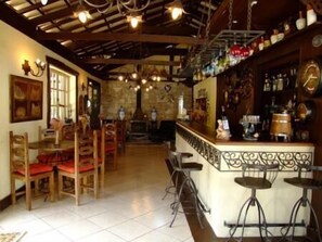 A bar area with wooden chairs and stools, a stone wall, and hanging lights. - Hospedaria da Villa (Tiradentes)