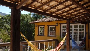 A wooden pergola with a yellow building, a hammock, and a potted plant. - Hospedaria da Villa (Tiradentes)