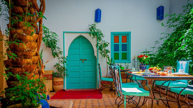 A traditional Moroccan interior with a tiled floor, a wooden door, and a dining area with a table set for two. - Riad Dar Mamouni (Marrakech)