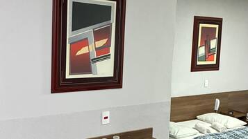 Habitación de hotel con un escritorio de madera y dos sillas, una cama con manta a cuadros azul y blanco, y dos cuadros abstractos en la pared.