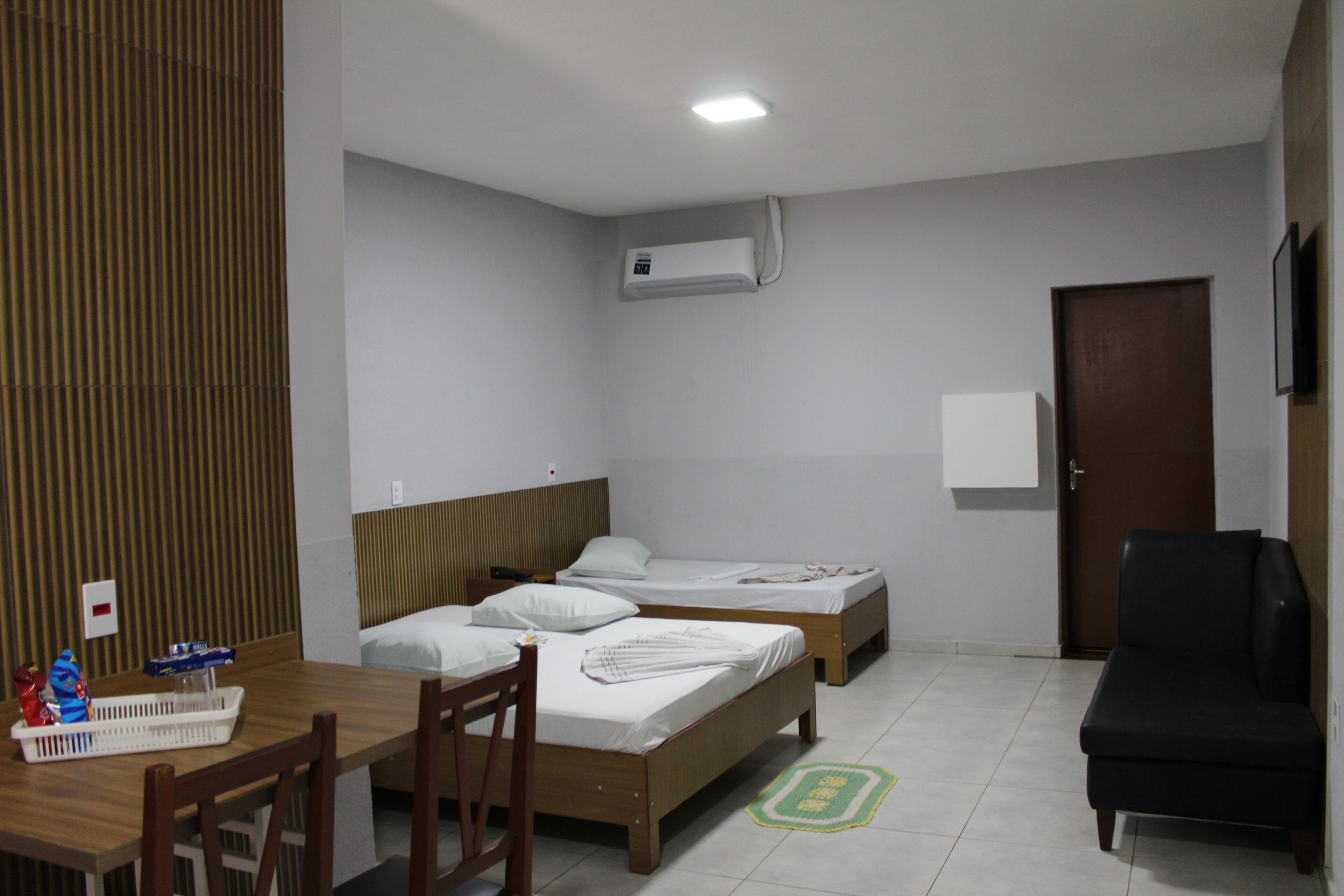 A hotel room with two beds, a desk, a chair, a TV, an air conditioning unit, and a door.