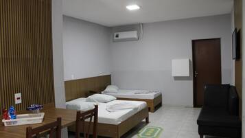 A hotel room with two beds, a desk, a chair, a TV, an air conditioning unit, and a door.