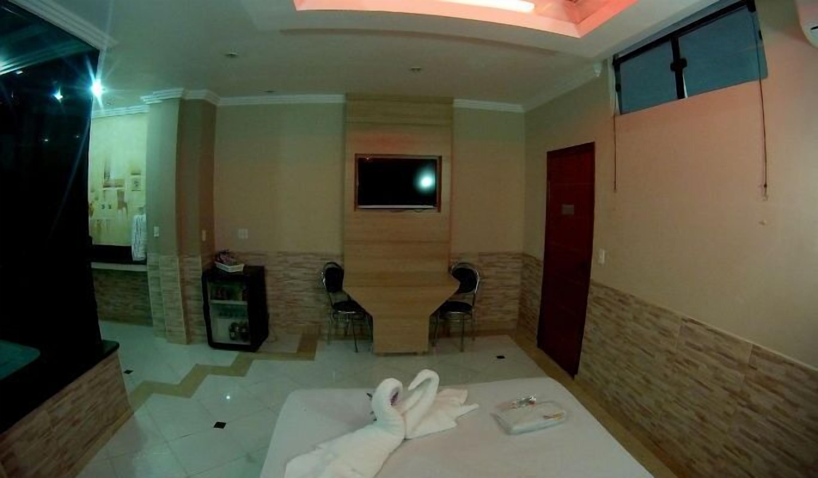 A hotel room with a bed, a TV mounted on the wall, a small table, and a red door.