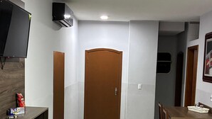Una sala de estar limpia y moderna con un televisor de pantalla plana, un mueble de madera, una mesa de comedor con sillas y una puerta al fondo.