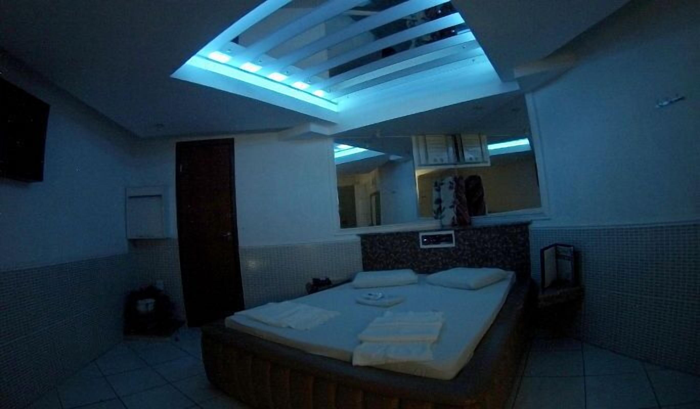 A bedroom with a bed, a bedside table, a mirror, and a window.