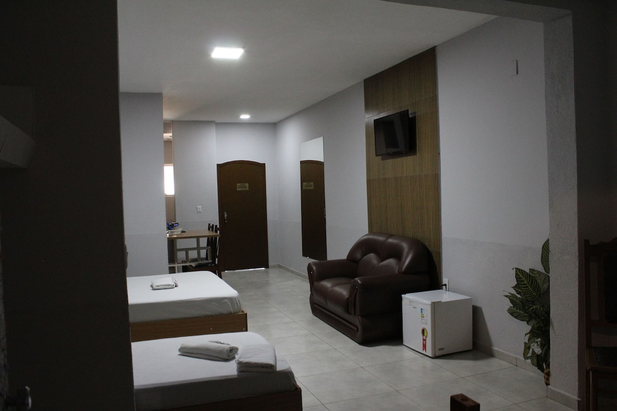 A hotel room with a bed, a sofa, a television mounted on the wall, and a small table with a chair.
