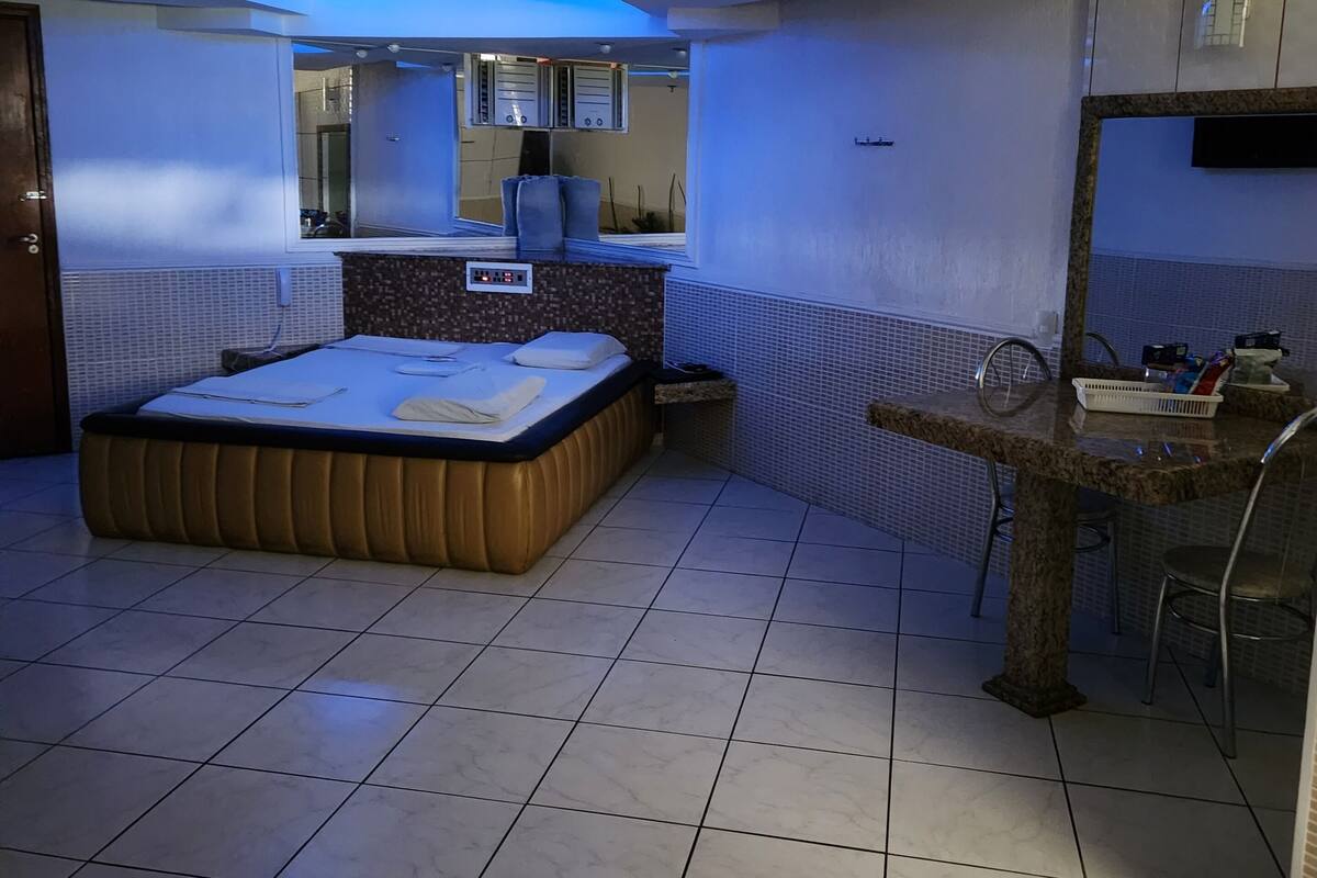 A bedroom with a bed, a small table, a chair, a mirror, and a window.