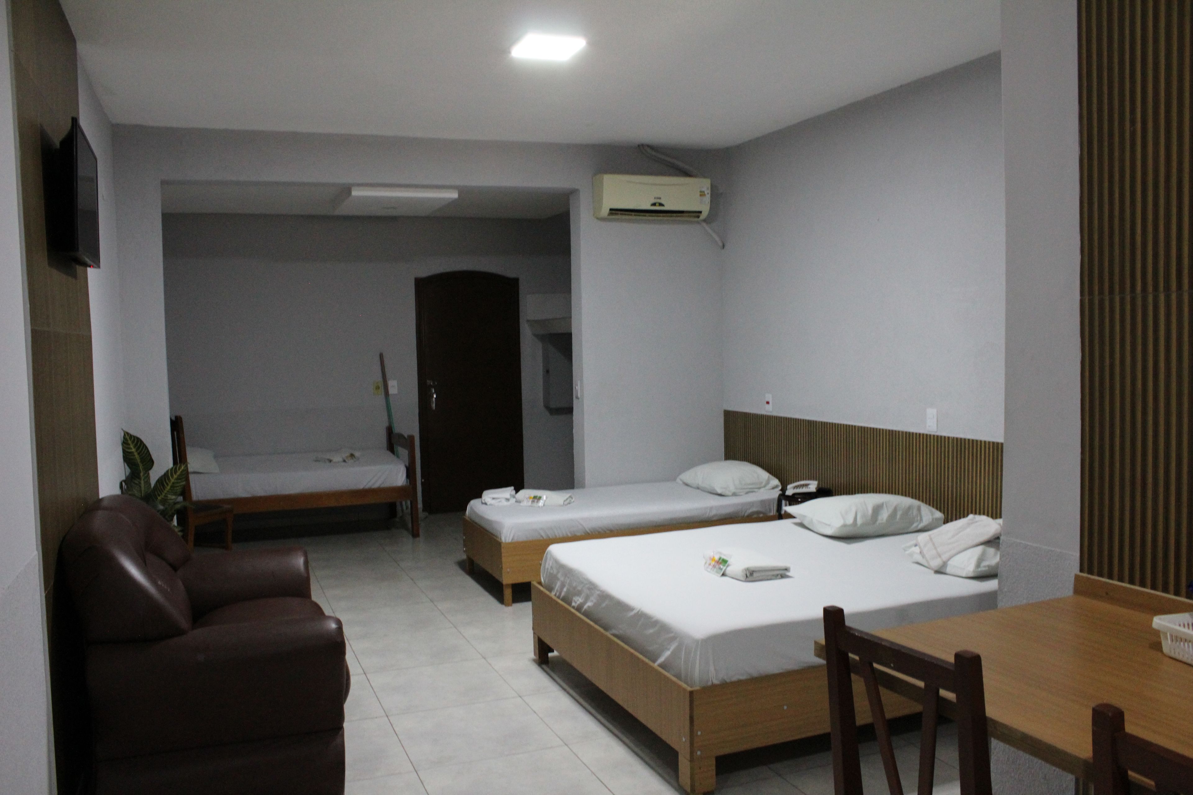 A hotel room with two beds, a desk, a chair, a TV, and a door leading to another room.