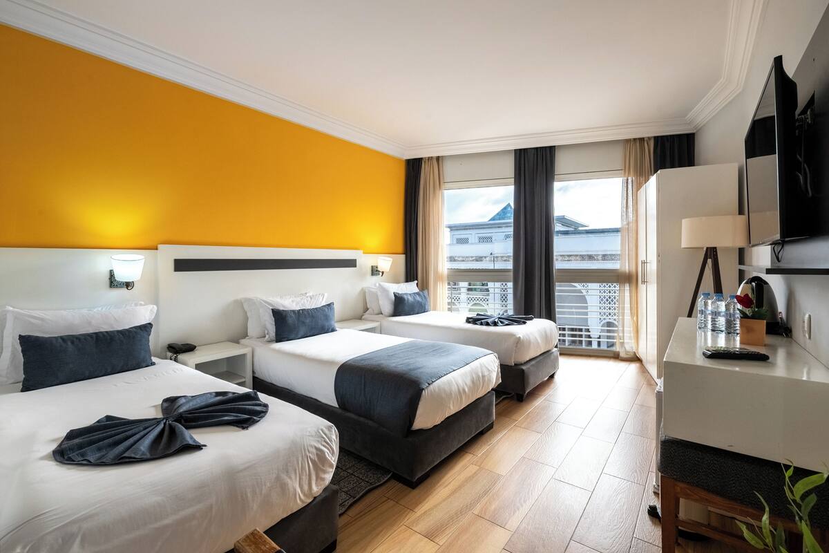 A hotel room with two beds, a desk, and a view of the sea.