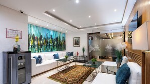 Een moderne woonkamer met een witte bank, een glazen salontafel en een kleurrijk abstract schilderij aan de muur.
