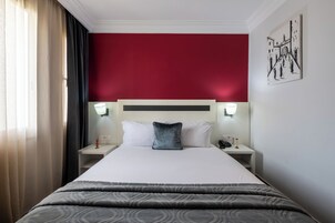 Una habitación de hotel con una cama grande, dos mesitas de noche, una pared de acento roja y una obra de arte colgada en la pared.