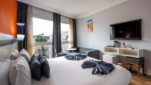 Een moderne hotelkamer met een groot bed, een televisie, een bureau en een balkon met uitzicht op de stad.