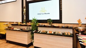 Een hotel receptie met een digitaal scherm, een buffet met diverse gerechten, en een plant.