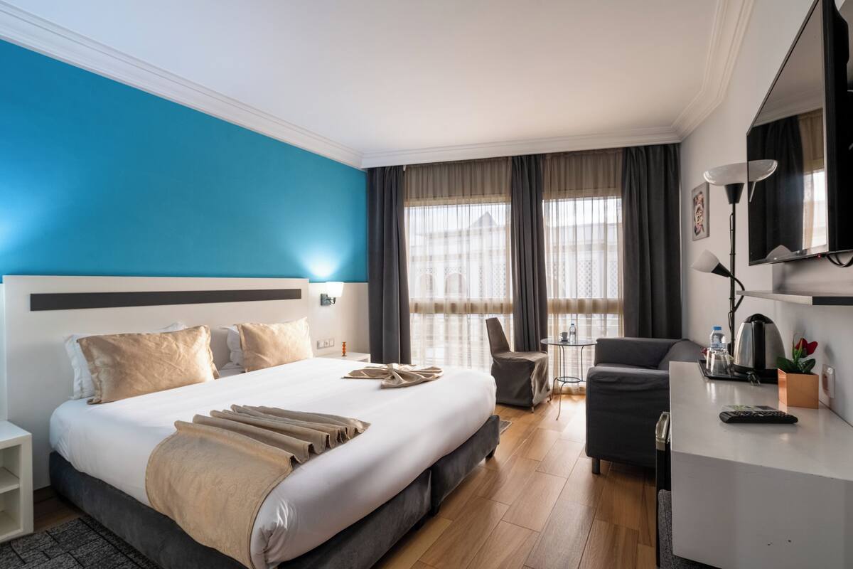 A hotel room with a large bed, a desk, a chair, and a view of the city through the window.