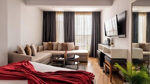 Een moderne hotelkamer met een bed, twee sofa's, een salontafel, een televisie en een klein bureau.