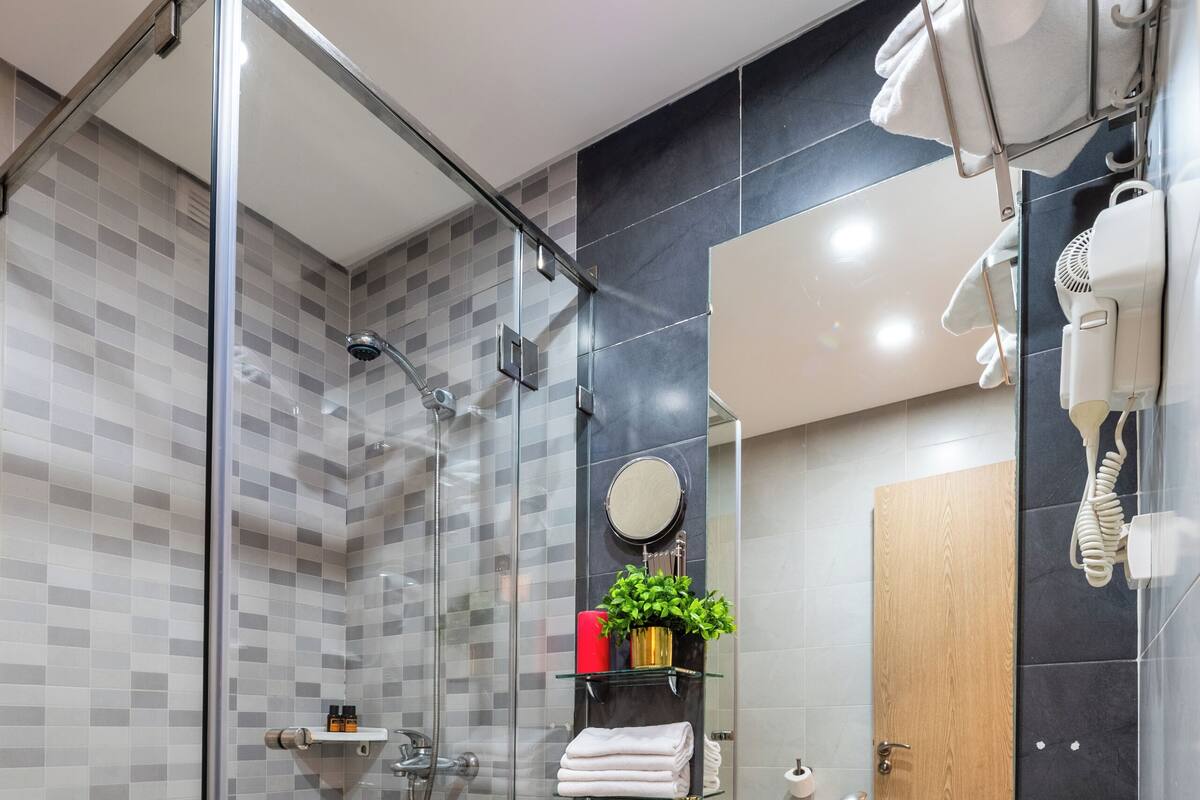 A modern bathroom with a glass-enclosed shower, a sink, a mirror, and a hairdryer.