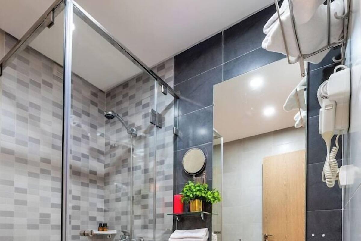 A modern bathroom with a glass shower enclosure, a sink, a mirror, and a towel rack.