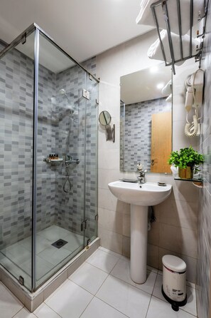 A modern bathroom with a glass-enclosed shower, a white sink, and a small trash bin.