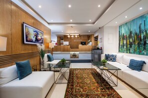A modern hotel lobby with a reception desk, white sofas, a large abstract painting, and a traditional patterned rug.