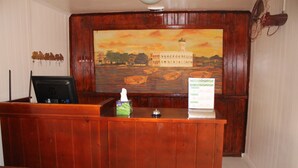 Un comptoir d’accueil en bois, avec un tableau représentant un bâtiment et des bateaux accroché au mur.