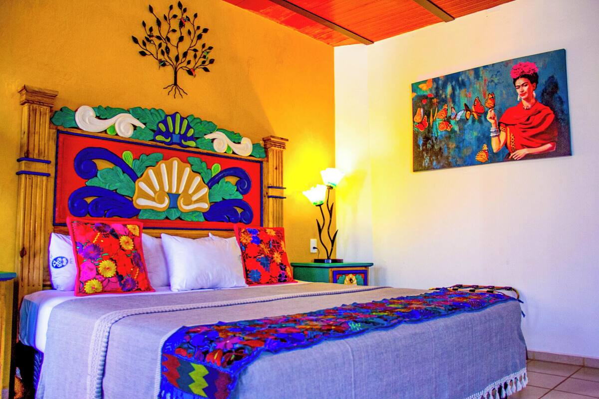 A bed with a colorful headboard, a painting on the wall, and a bedside lamp.