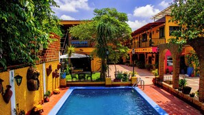 A swimming pool surrounded by colorful buildings, a covered seating area, and various potted plants. - Posada Margaritas (Tlaquepaque)