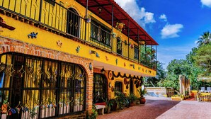 A two-story building with a red roof, yellow walls, and a balcony with potted plants. - Posada Margaritas (Tlaquepaque)