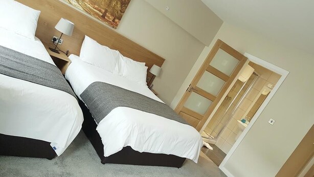 A hotel room with two beds, a wooden headboard, a painting, a nightstand, and a door leading to a bathroom. - Belfast House (Cookstown)