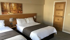 A hotel room with two beds, a large painting of a forest, a wooden headboard, and a door with a glass panel. - Belfast House (Cookstown)