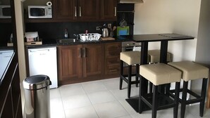 A compact kitchen with wooden cabinets, a microwave, a sink, and a small dining area with stools. - Belfast House (Cookstown)