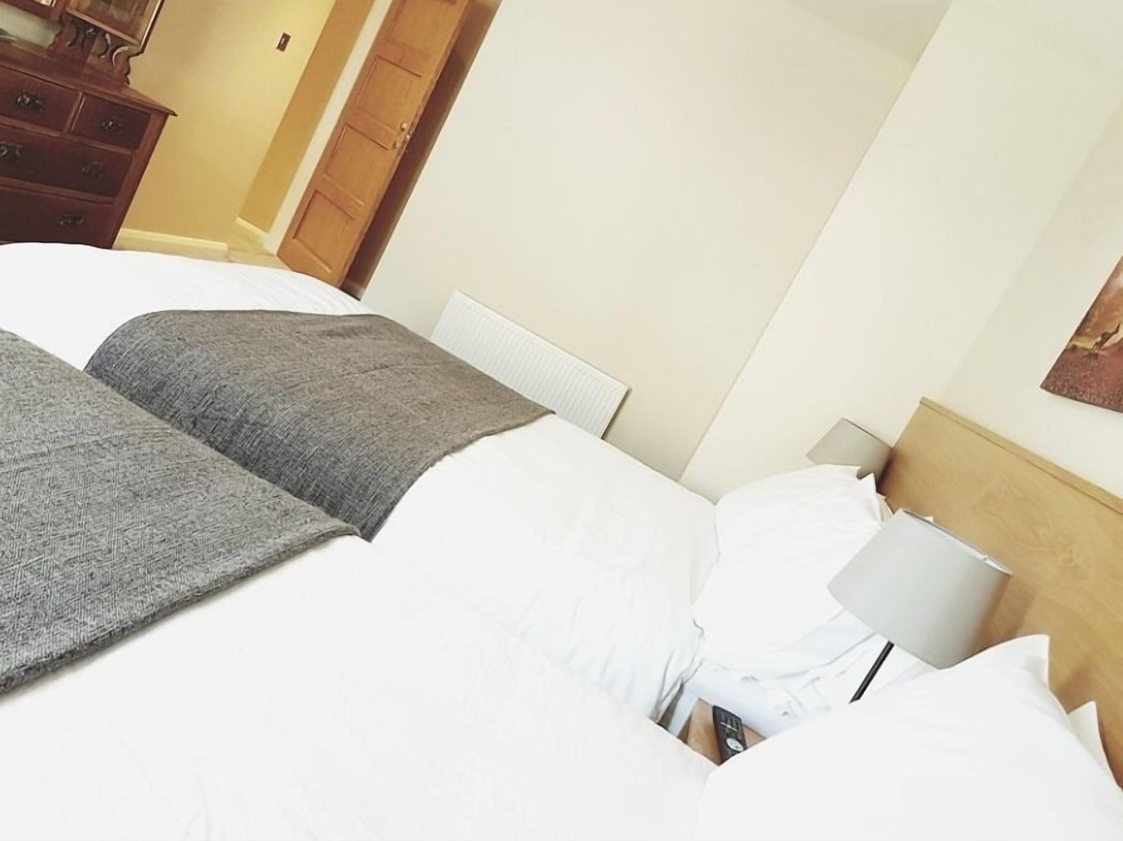 Quarto de hotel com uma cama grande, uma cômoda de madeira e uma mesa de cabeceira com abajur.