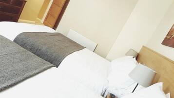 Quarto de hotel com uma cama grande, uma cômoda de madeira e uma mesa de cabeceira com abajur.