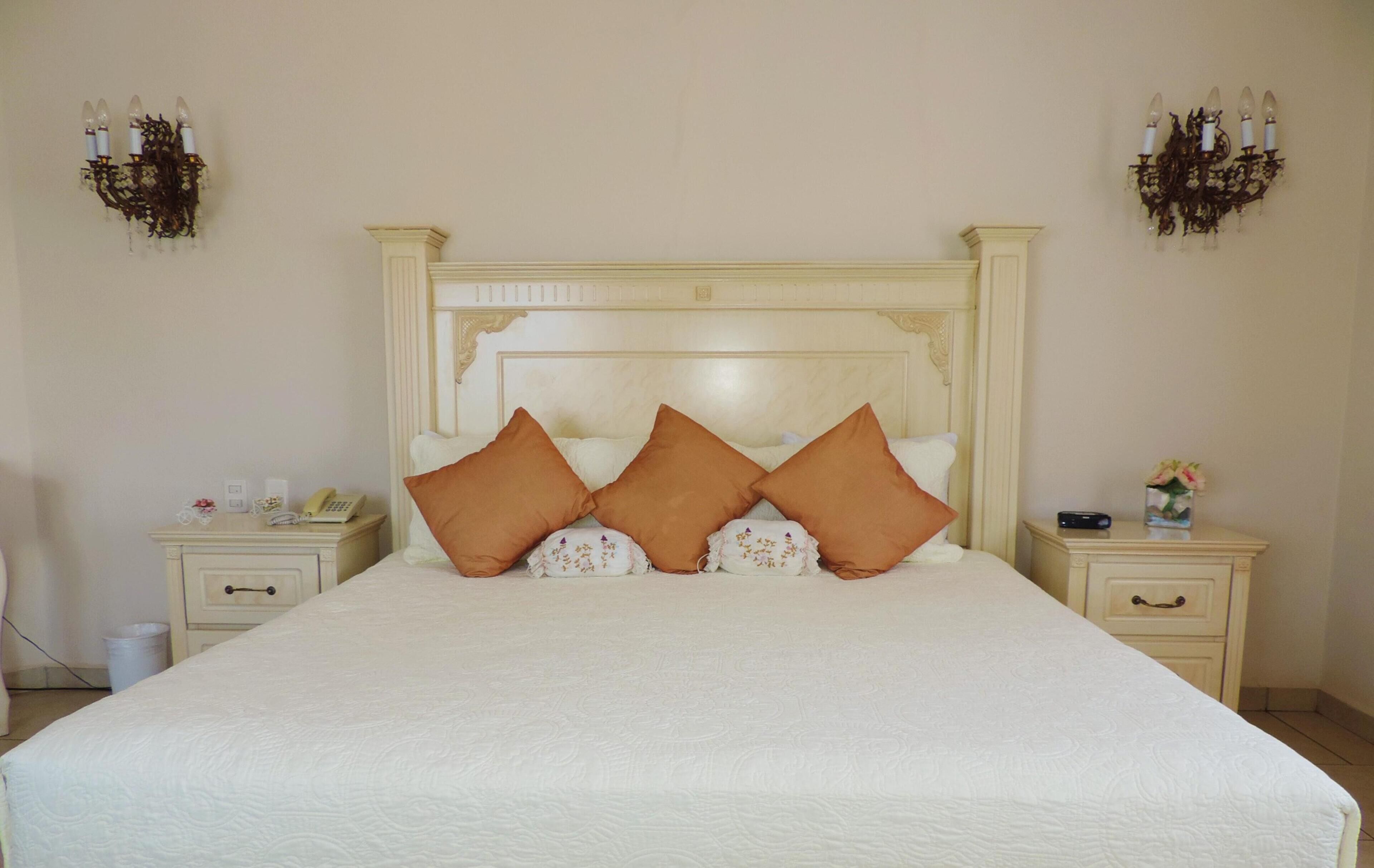 Une chambre à coucher avec un grand lit, deux tables de chevet, une commode, une lampe fixée au mur et un applique décorative.