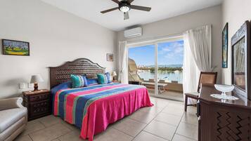 Une chambre d’hôtel avec un lit, un bureau, une chaise, un ventilateur de plafond et une vue sur la mer.