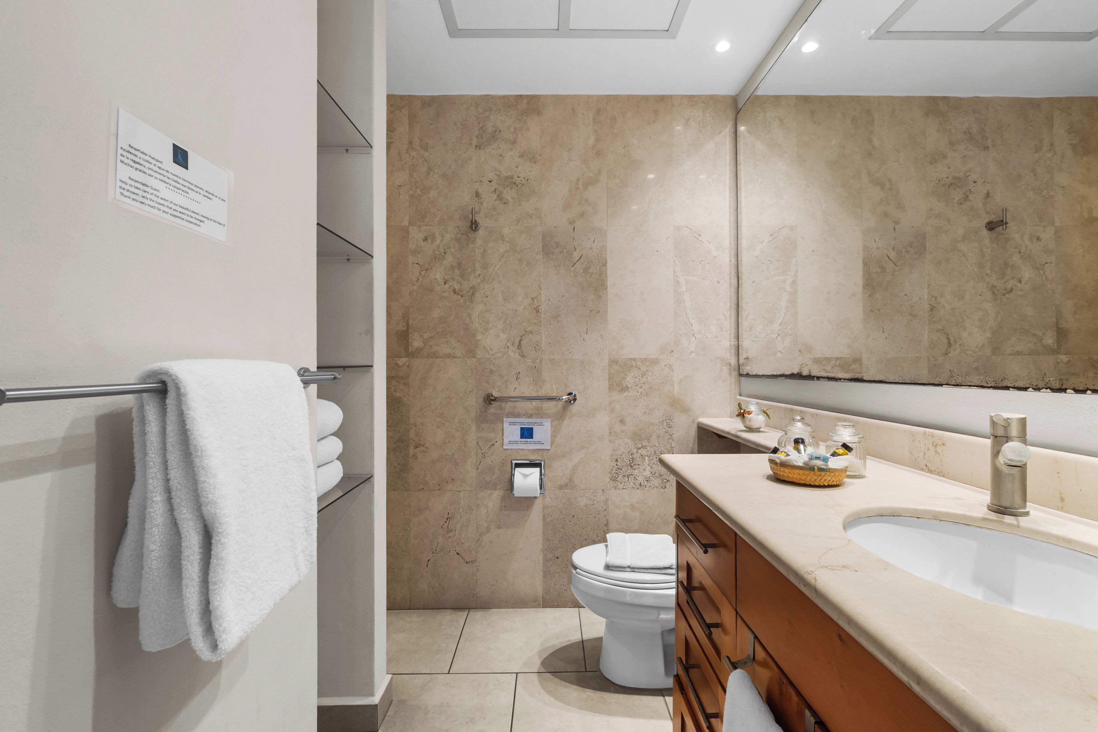 A modern bathroom with a beige tiled wall, a white toilet, a sink with a mirror, and a towel rack.