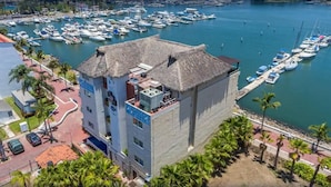 Un edificio de varios pisos con tejado de paja, situado cerca de un puerto deportivo con numerosos barcos amarrados.