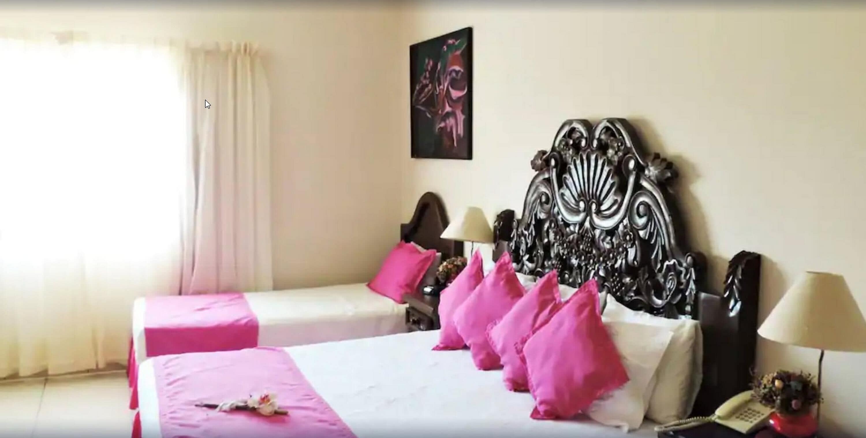 Ein Hotelzimmer mit zwei Betten, jeweils mit rosa Bettwäsche, einem dekorativen Kopfteil und einem Bild an der Wand.