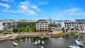 A coastal hotel with multiple balconies, a marina with several boats, and a backdrop of urban buildings. - Marina Banderas Suites (Nuevo Nayarit)